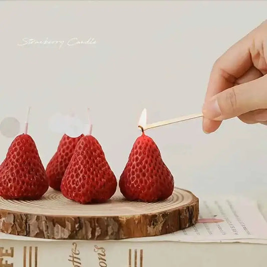 Cute strawberry candles for parties being lit with a match on a wooden slice.
