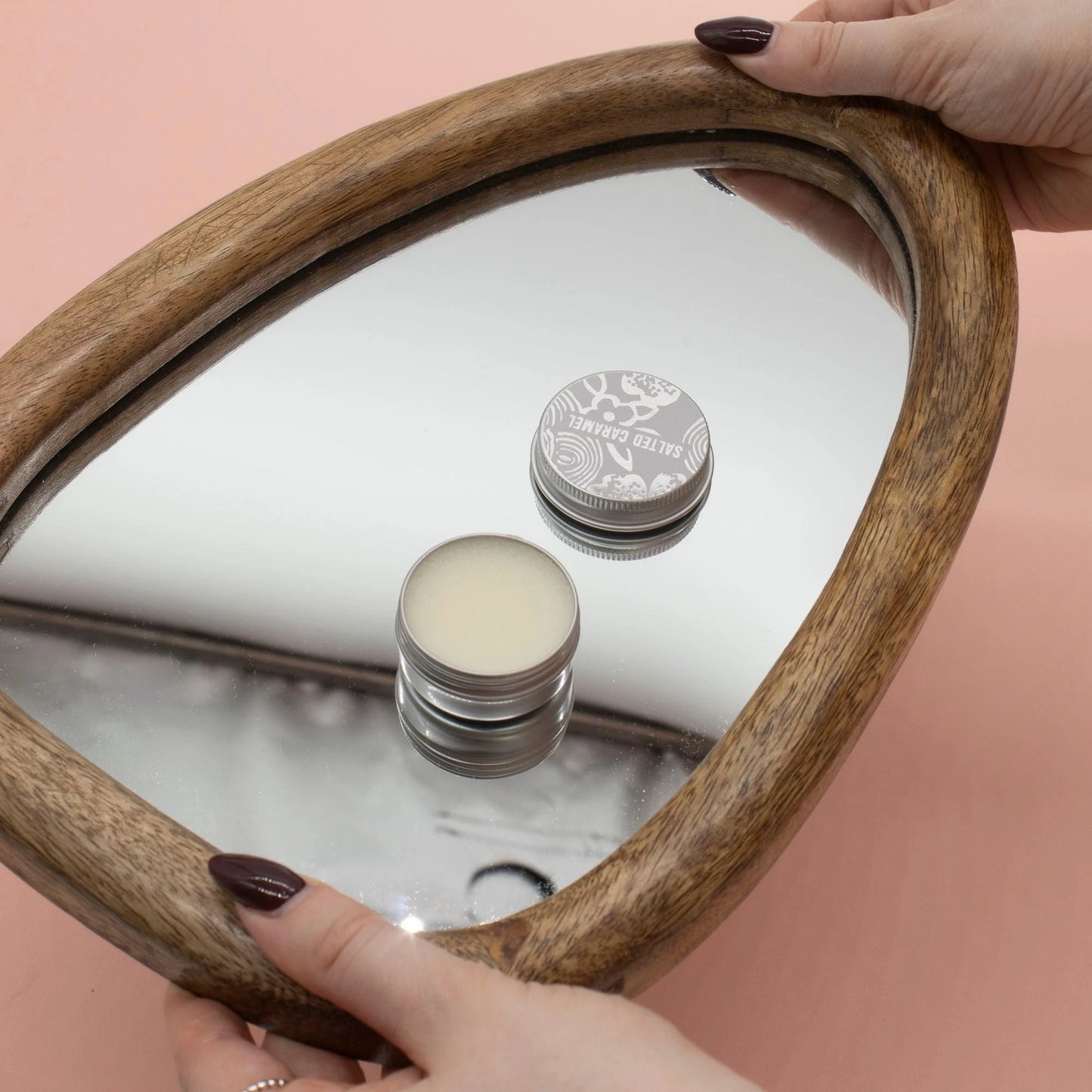 Agnes + Cat Pinacolada lip balm tin reflected in a wooden mirror, showcasing the creamy lip balm for soft lip comfort.
