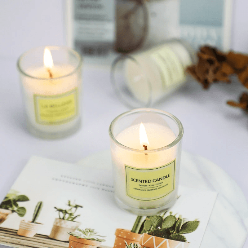 Small glass cup aromatherapy soy wax candles lit on a stylish table with decor and plants.