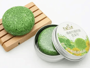 Natural plant-based hair soap in green color on a wooden soap dish and in a silver tin.