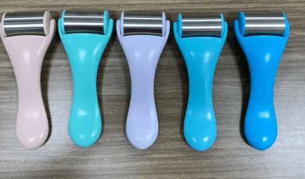 Variety of colorful stainless steel facial massage tools lined up on a wooden surface.