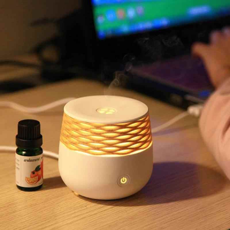 Portable ultrasonic aromatherapy diffuser with warm light and essential oil bottle on desk.