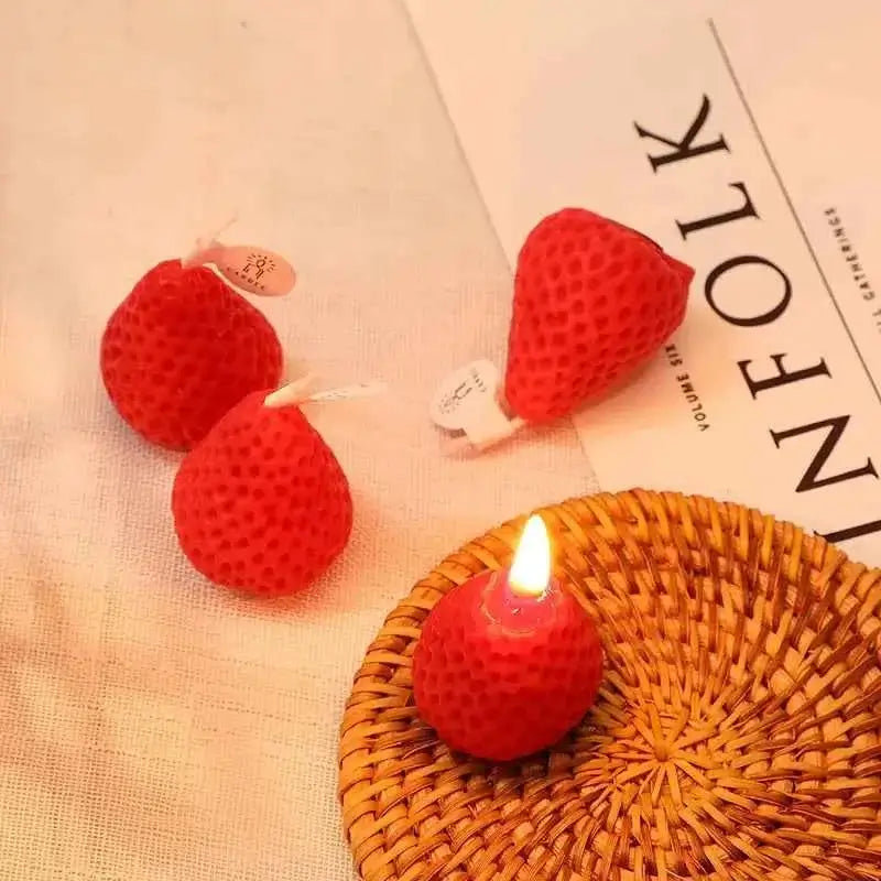 Cute strawberry candles for parties displayed on a woven plate, featuring charming strawberry shapes and a lit candle.