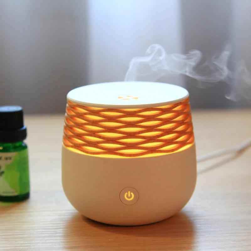 Portable ultrasonic aromatherapy diffuser emitting mist with warm light and essential oil bottle beside it.