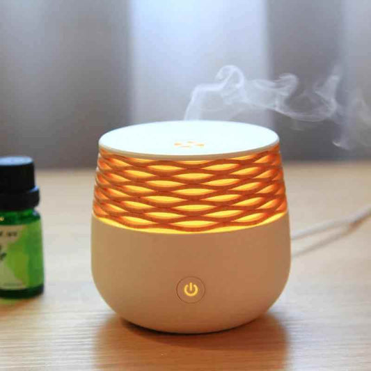 Portable ultrasonic aromatherapy diffuser emitting mist with warm light and essential oil bottle beside it.