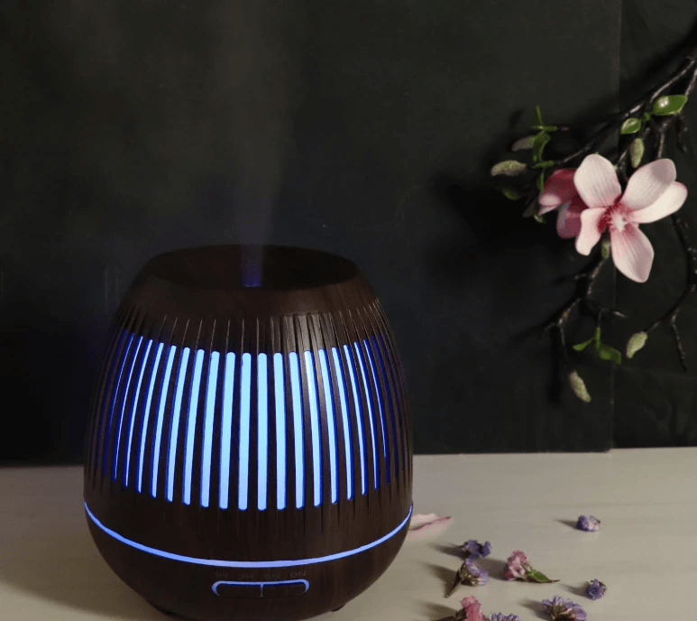 Aromatherapy humidifier with LED lights emitting mist and glowing blue, set against a dark background with flowers.