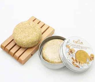Natural plant-based hair soap, Ginger Hair Soap, displayed on a wooden soap dish with its tin packaging.