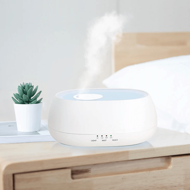 Aromatherapy diffuser humidifier lamp emitting mist on a nightstand next to a small plant.